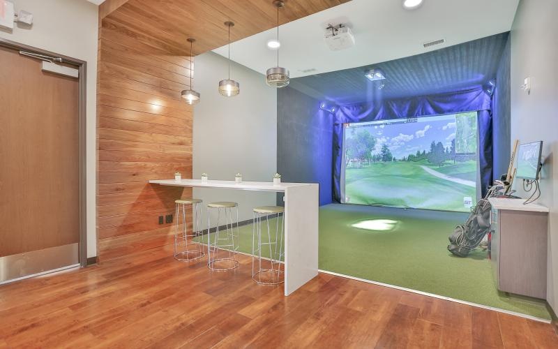 a room with a golf simulator tables and chairs