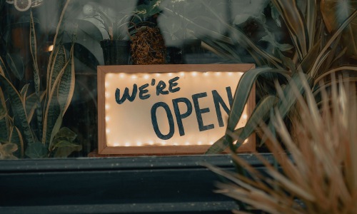 Close to the center of everything We're Open sign on a window ledge, surrounded by plants