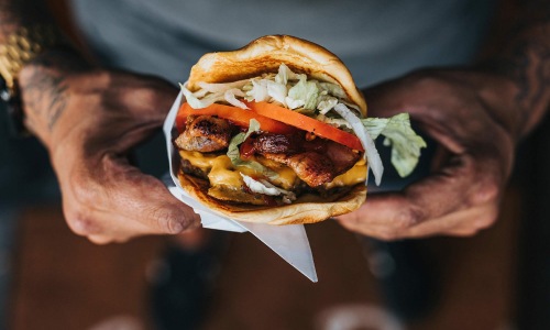 Bustling community with plenty of dining choices man holds a thick, juicy burger with both hands